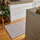 A rectangular area rug with a gray and white herringbone pattern, placed on a light wood floor in a modern kitchen setting.