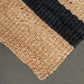 Close-up of a woven rug with beige and black stripes on a gray background
